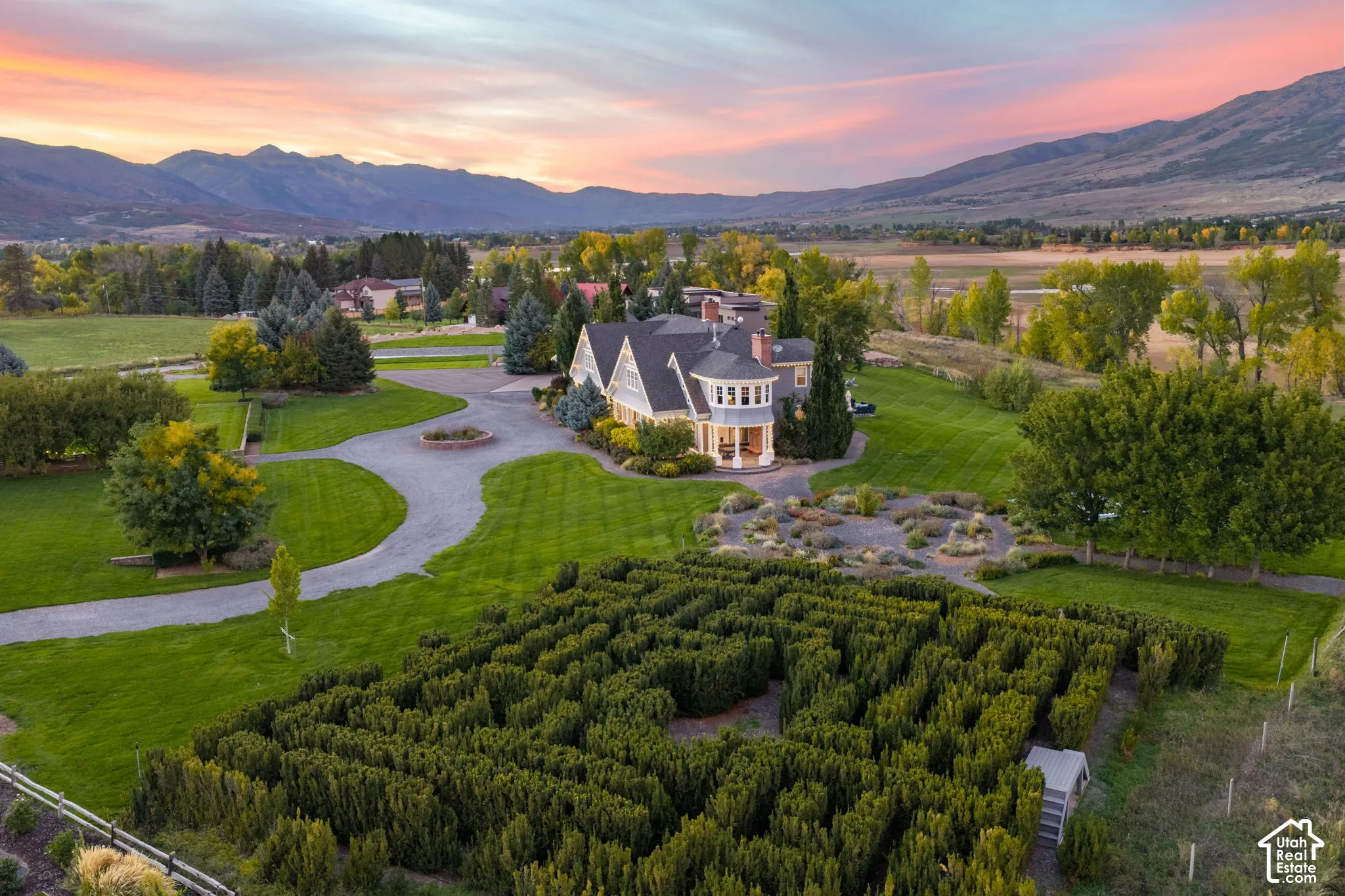 Multi-gabled estate residence featuring a formal hedge maze, extensive manicured grounds, circular gravel driveway, and mountain backdrop