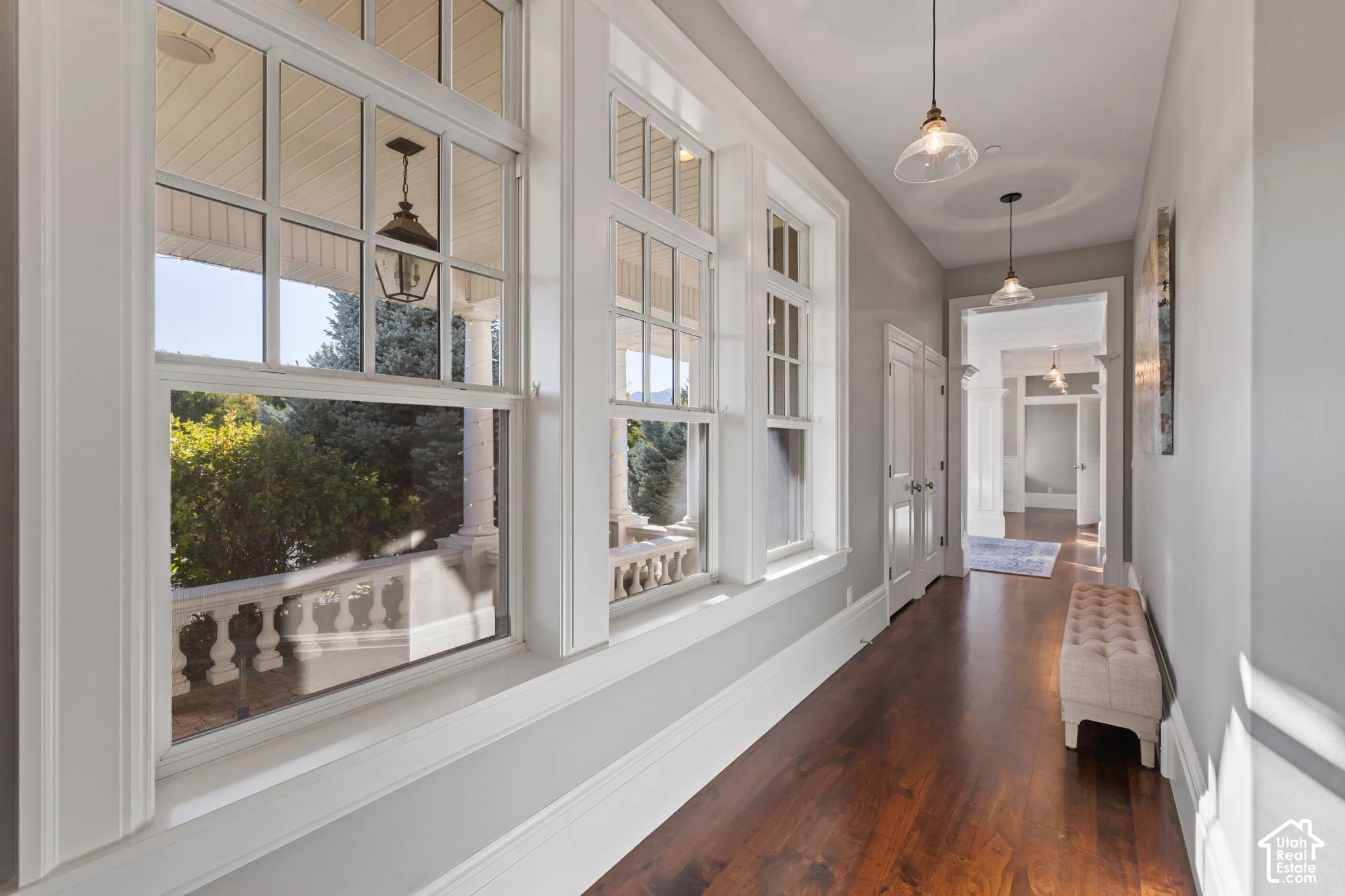 Hallway featuring wood-finish flooring, tall multi-pane windows, crown molding, and pendant lighting