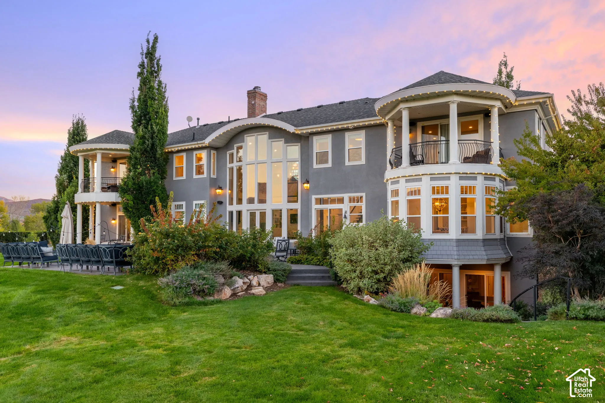 Multi-level exterior featuring floor-to-ceiling windows, dual wraparound balconies with decorative iron railings, and tiered landscaping