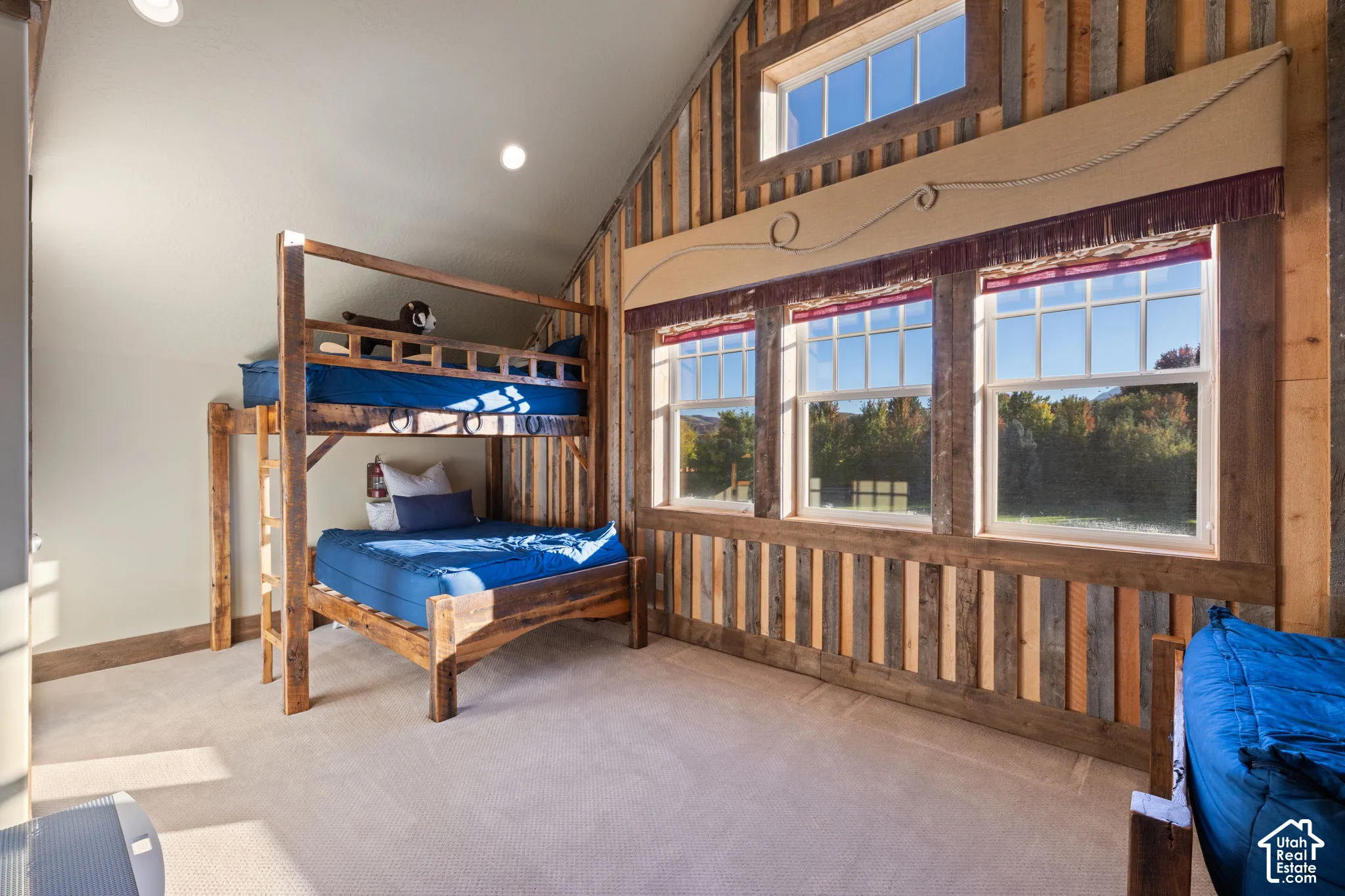 Bunkroom with built-in beds, vaulted ceiling, vertical wood-plank wall paneling, multiple large windows, and recessed lighting