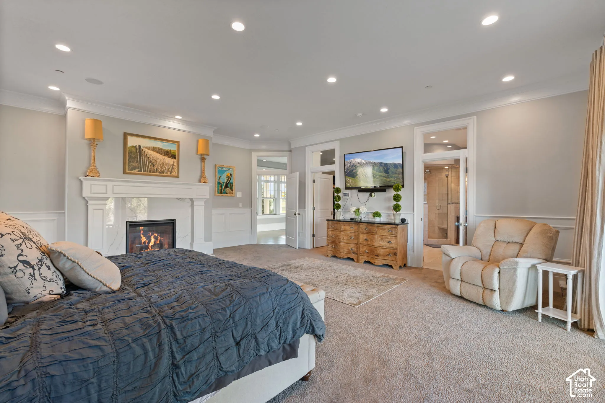 Luxurious primary suite featuring a gas fireplace with decorative mantel, recessed ceiling lighting, and carpet flooring throughout