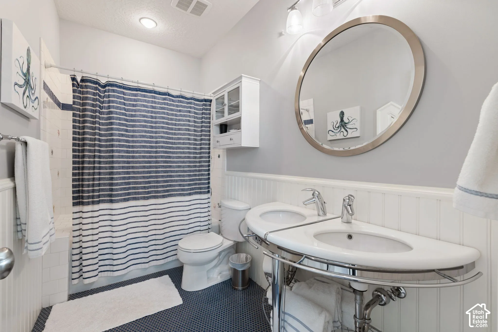 Double vanity with integrated sinks, chrome fixtures, circular mirror, beadboard wainscoting, and built-in wall cabinetry