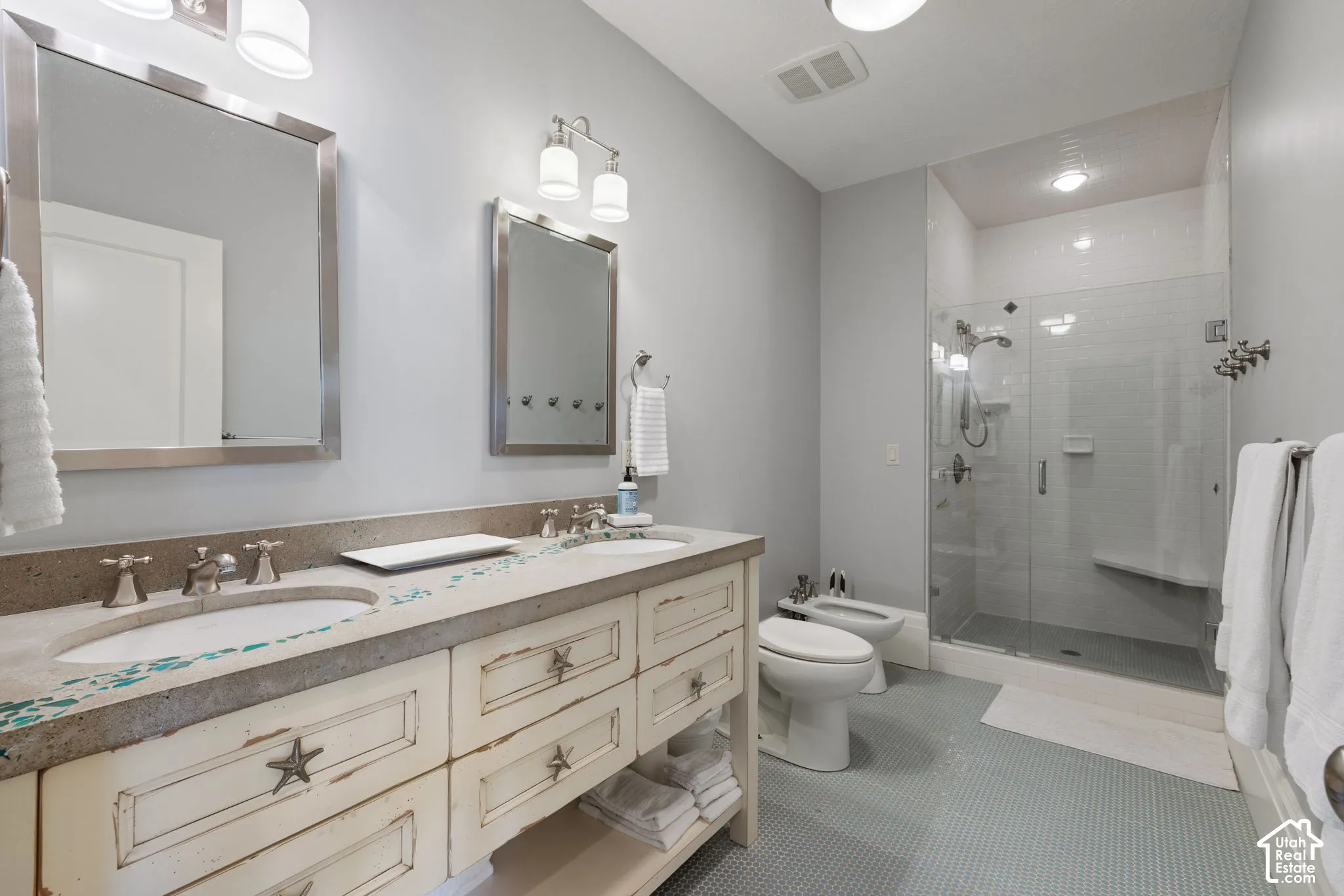 Double vanity with dual under-mount sinks and stone countertops, glass-enclosed walk-in shower with integrated bench seating, and ceramic tile flooring