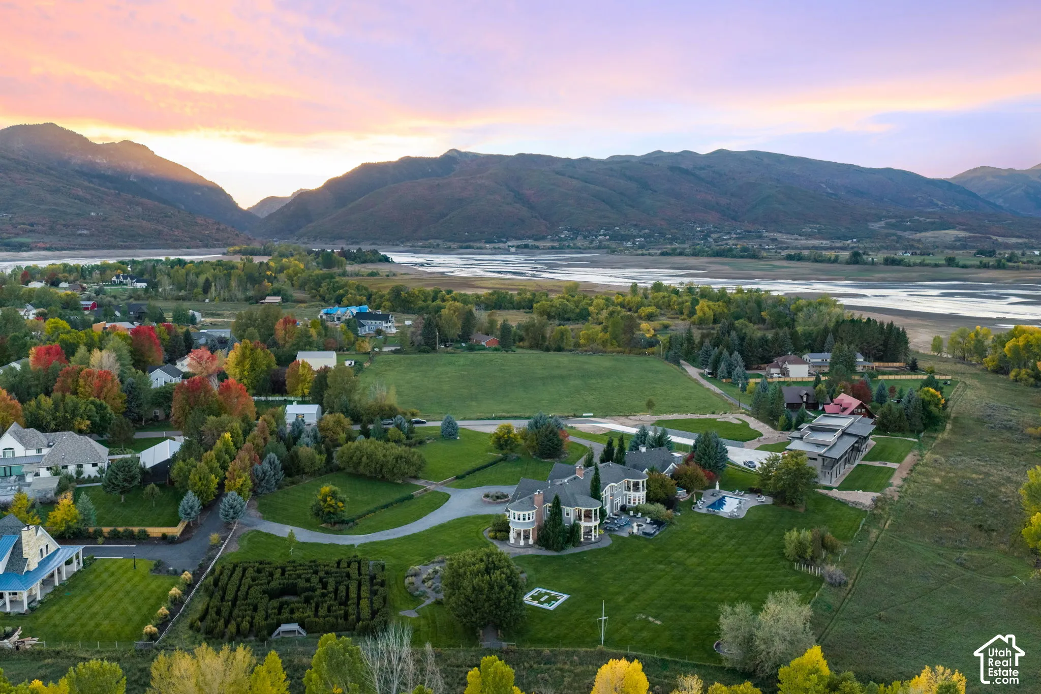 Extensive estate grounds featuring a hedge maze, paved circular driveway, stone exterior architecture, mountain backdrop, and proximity to water