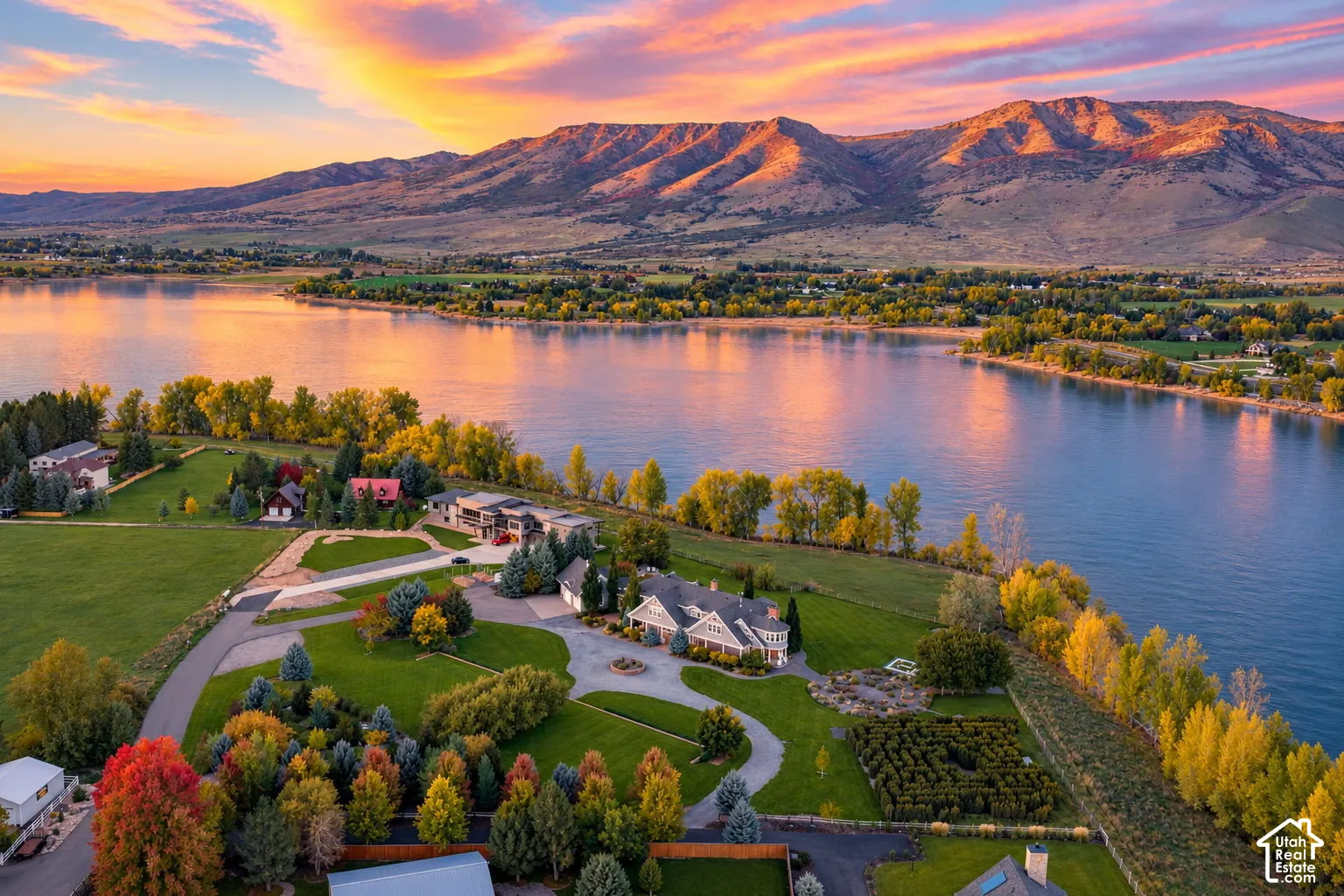 Aerial perspective of a sprawling waterfront estate featuring expansive lawns, mature trees, paved circular driveway, and dramatic mountain backdrop. Accurate AI generated depiction of the reservoir at full capacity. Currently drained for pipeline repair.