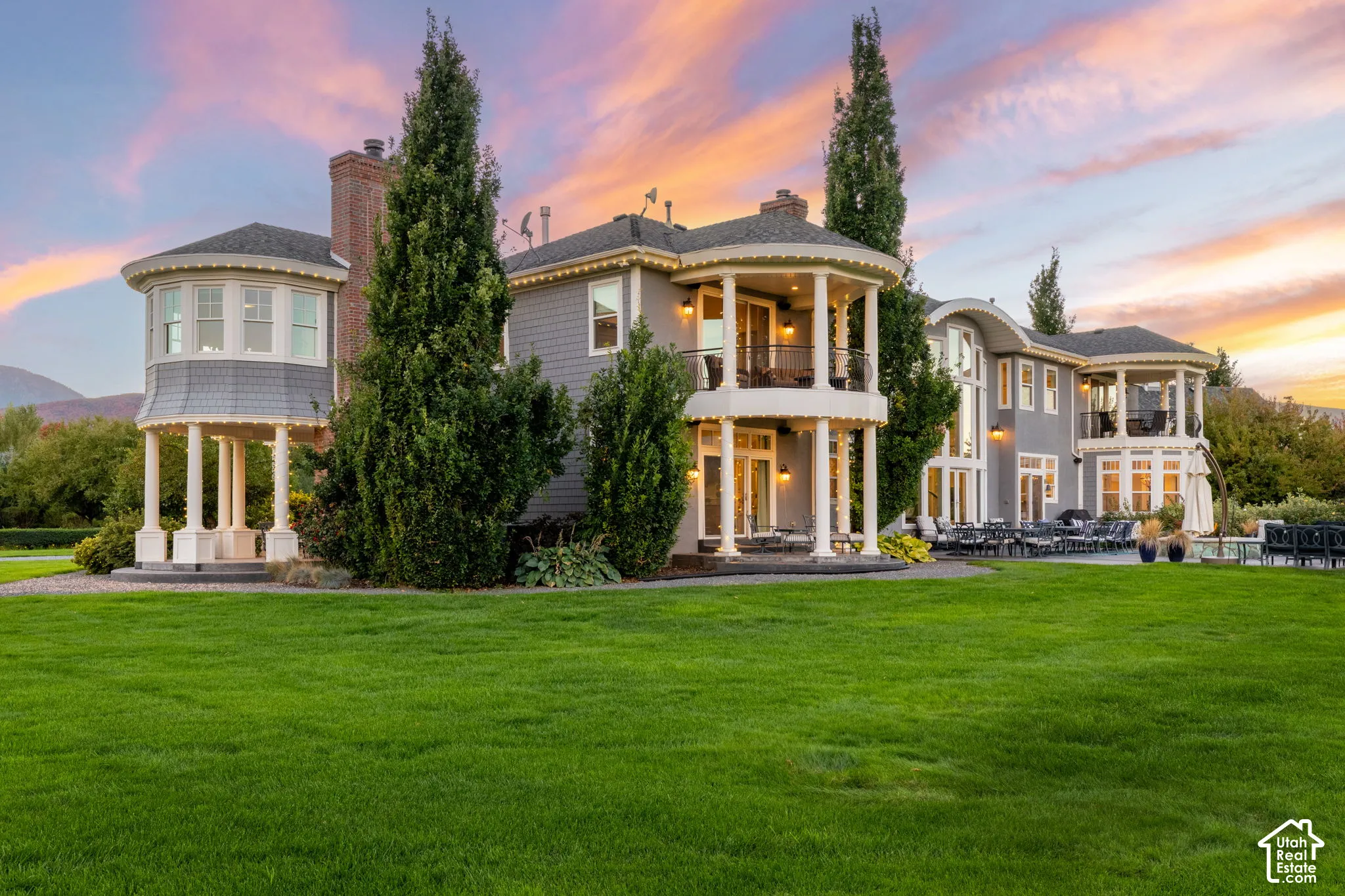 Multi-story residence featuring shingle siding, wrap-around columned porches, multiple balconies, a brick chimney, and an expansive manicured lawn