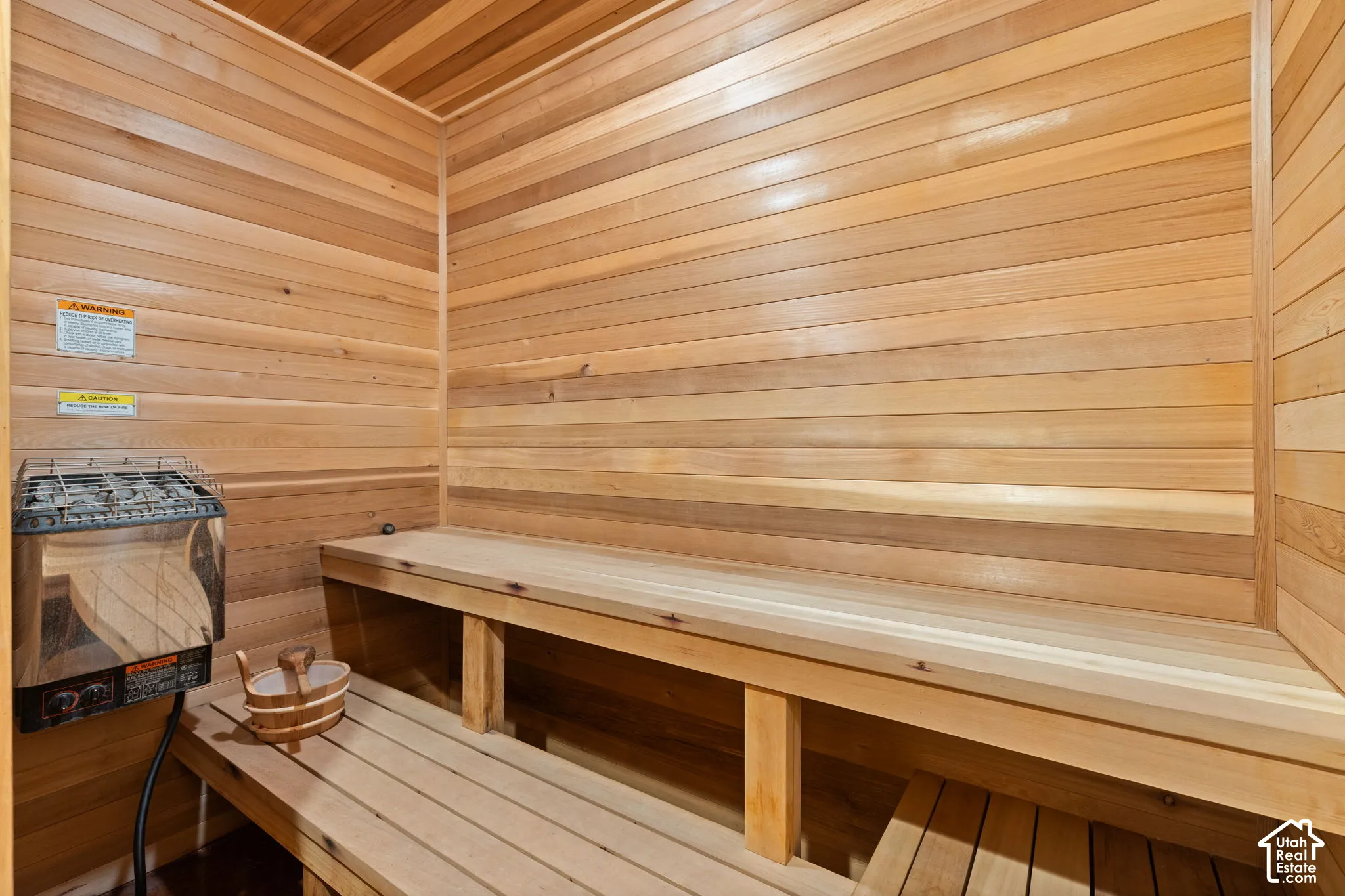 Sauna room featuring wood-paneled walls, multi-level built-in wooden benches, and an integrated heater