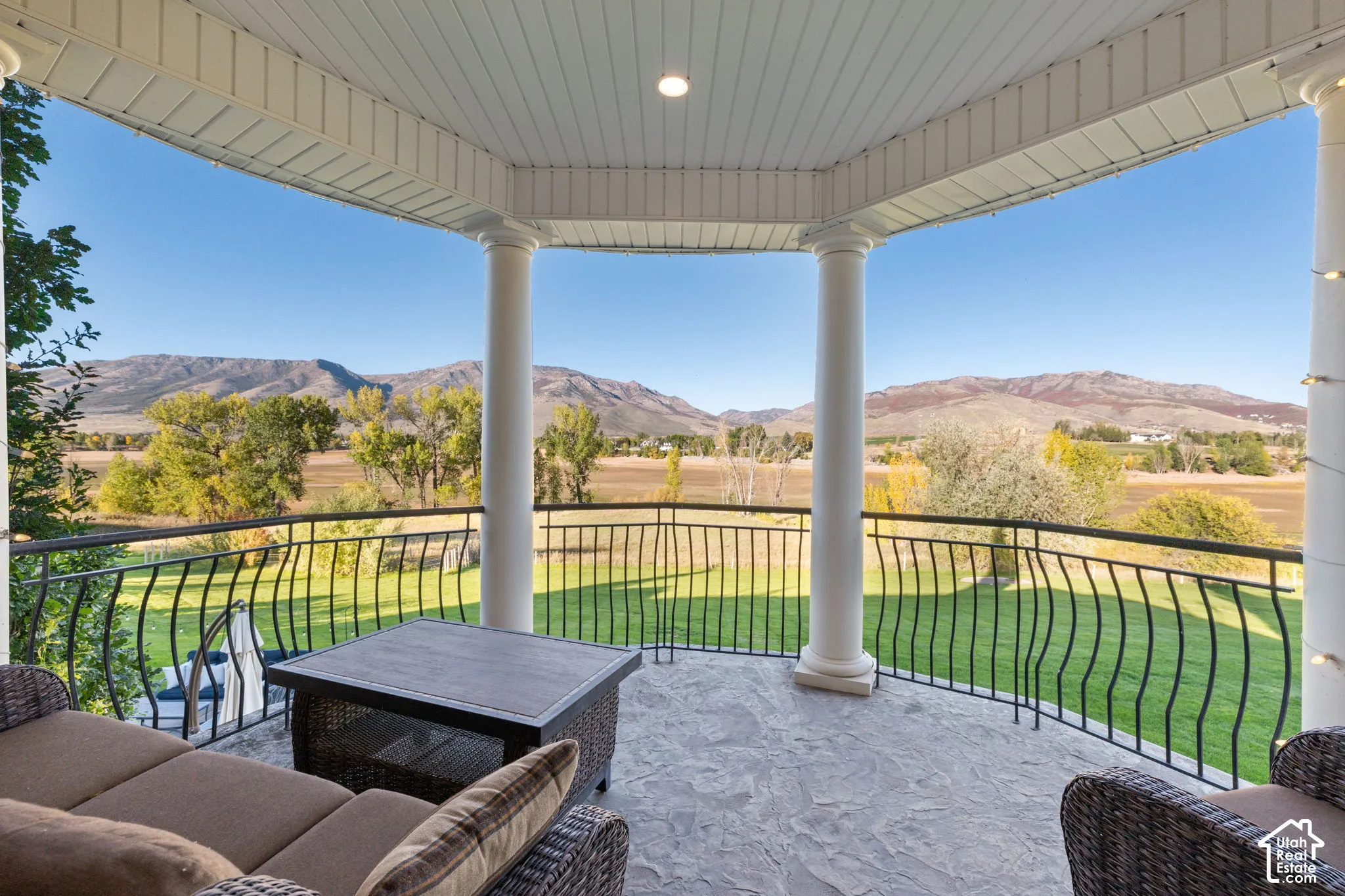 Covered balcony featuring stone flooring, classic architectural columns, and metal railing overlooking mountainous terrain and Pineview Reservoir.