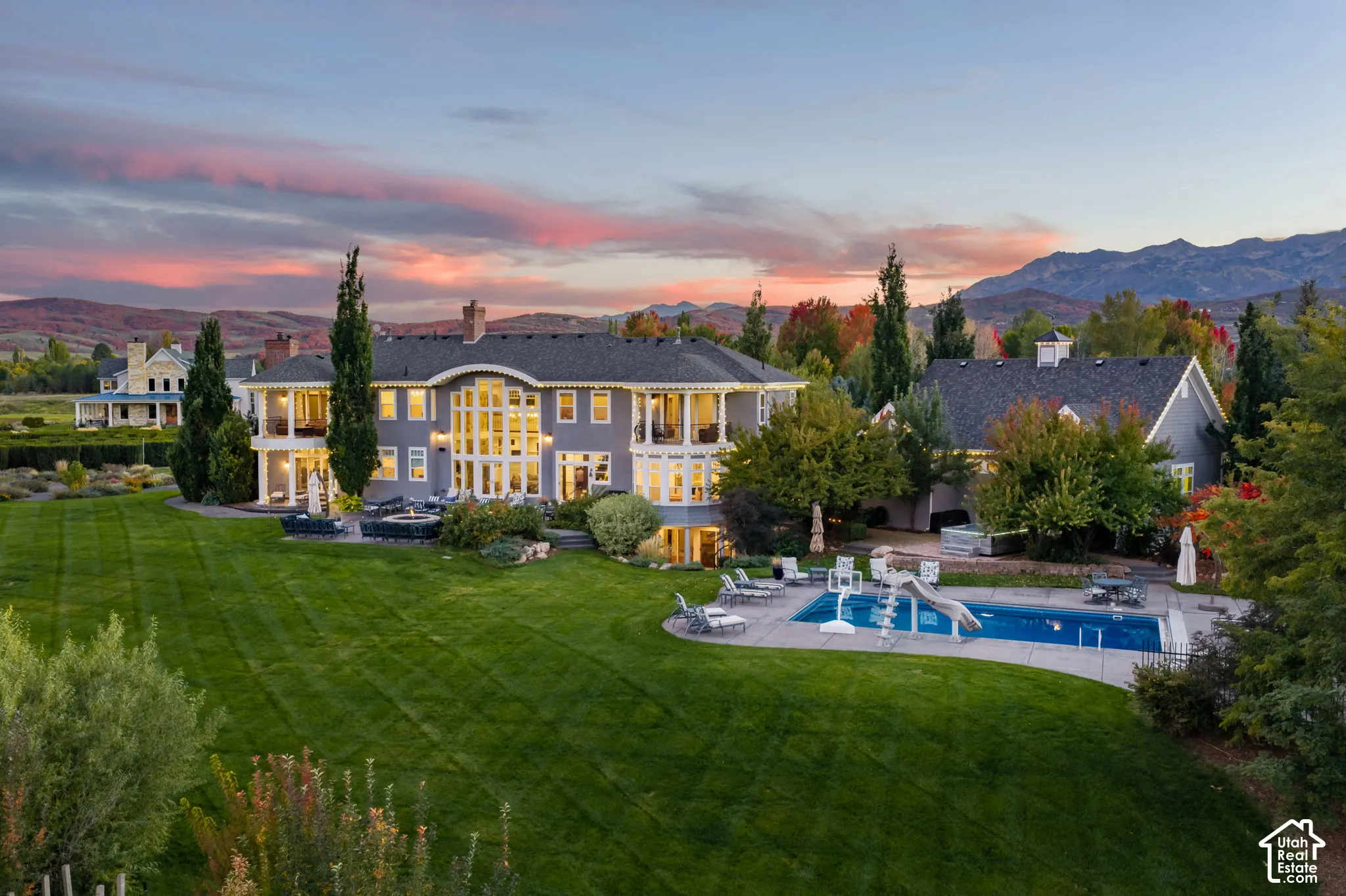 Classic Cape Cod two-story residence featuring a multi-pane window facade, wrap-around covered porches, an in-ground swimming pool with a slide, and expansive landscaped grounds set against a mountain backdrop