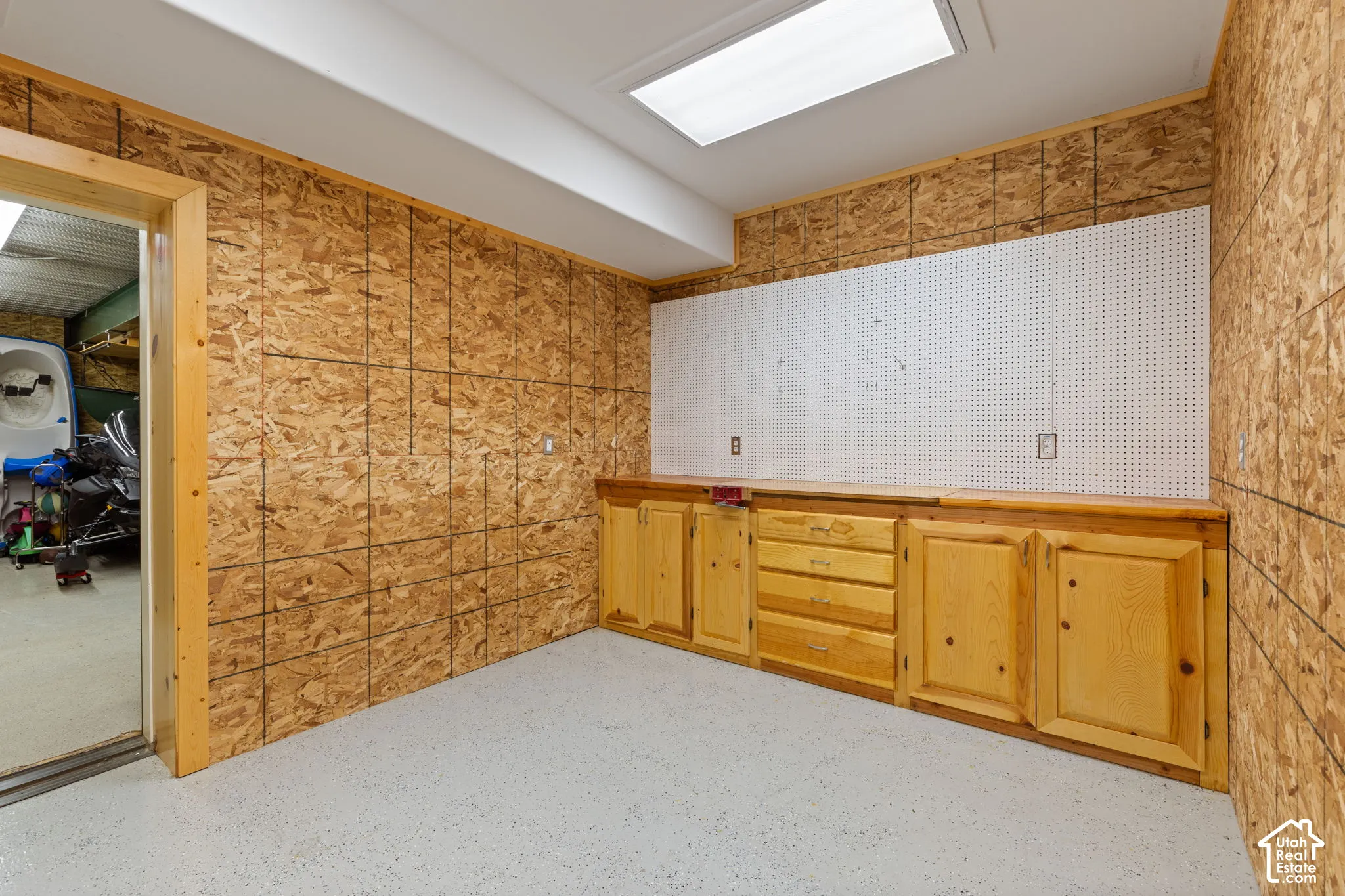 Versatile storage with wall paneling, built-in wooden cabinetry with multiple storage compartments, white pegboard backing, recessed lighting, and epoxy flooring
