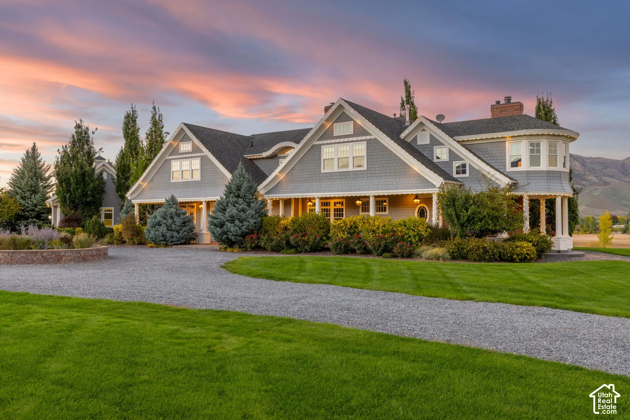 Multi-gabled exterior featuring shingle siding, a wraparound covered porch with column supports, a curved turret, and a stone-lined gravel driveway