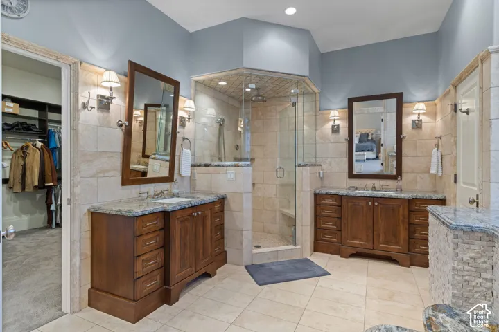 Dual-vanity bathroom featuring custom wood cabinetry, stone countertops, glass-enclosed shower with tiled surround, and wall-mounted sconce lighting