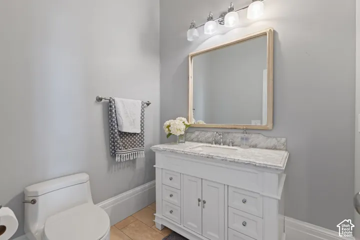 White vanity with stone countertop, undermount sink, framed wall mirror, and four-light overhead fixture