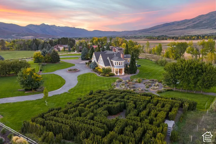 Multi-gabled estate residence featuring a formal hedge maze, extensive manicured grounds, circular gravel driveway, and mountain backdrop