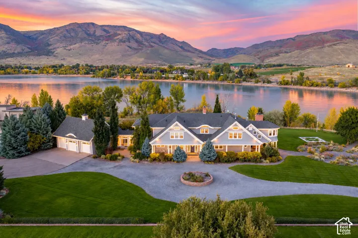 Waterfront residence featuring a multi-gabled architectural roofline, circular gravel drive, attached multi-car garage, and expansive lawn under a mountain backdrop. AI generated depiction of the reservoir at full capacity. Lake is currently drained for r
