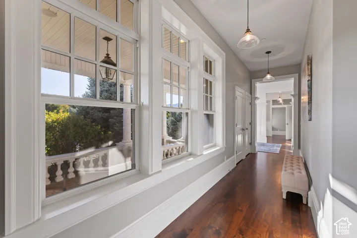 Hallway featuring wood-finish flooring, tall multi-pane windows, crown molding, and pendant lighting