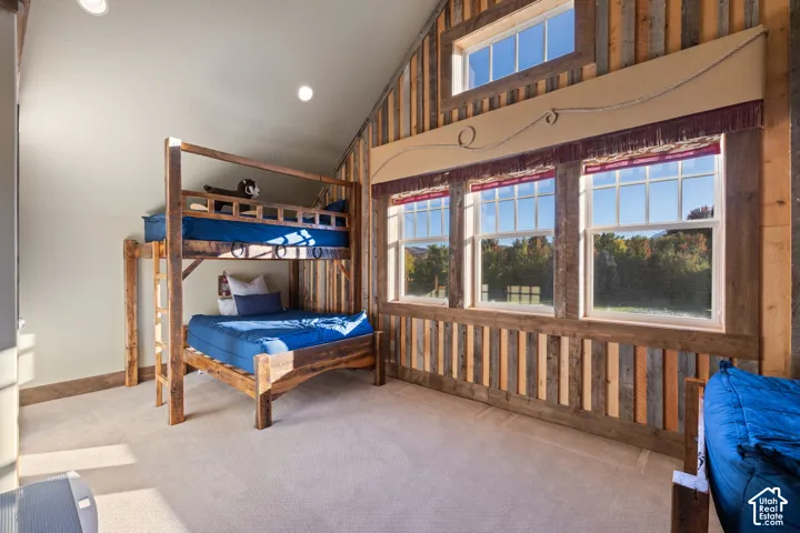 Bunkroom with built-in beds, vaulted ceiling, vertical wood-plank wall paneling, multiple large windows, and recessed lighting