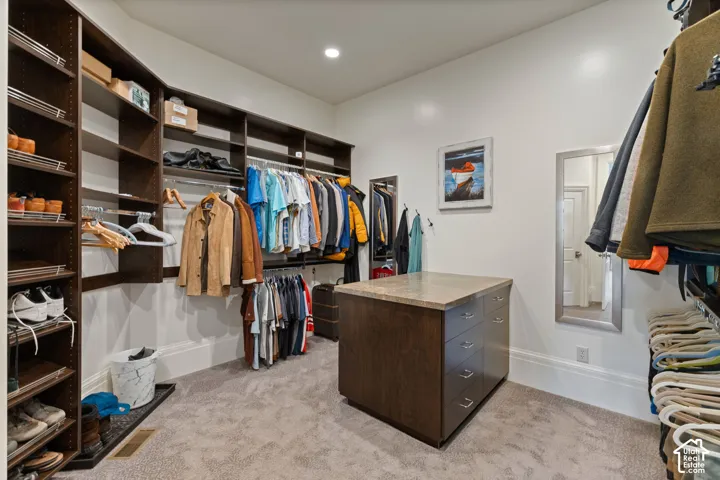 Walk-in closet featuring extensive dark wood-finish cabinetry, floor-to-ceiling shelving, built-in drawer island with stone-finish countertop, and recessed ceiling lighting