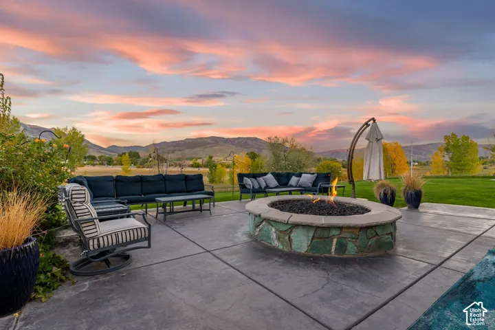 Stamped concrete patio featuring a circular stone-veneer fire pit, expansive lawn, and mountain backdrop