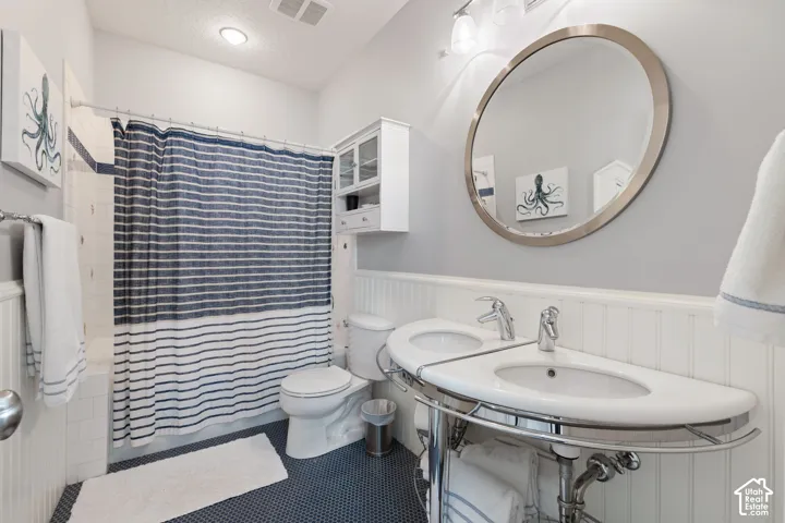 Double vanity with integrated sinks, chrome fixtures, circular mirror, beadboard wainscoting, and built-in wall cabinetry