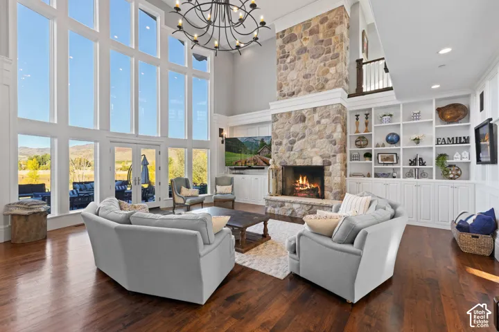 Double-height windows, floor-to-ceiling stone fireplace, built-in custom shelving, wood-finish flooring, and multi-tier iron chandelier