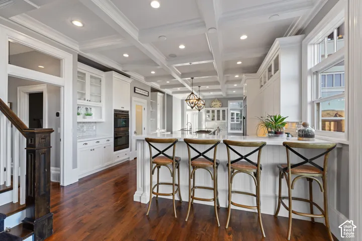 Coffered ceilings, custom white cabinetry, recessed lighting, double wall ovens, and wood-finish flooring