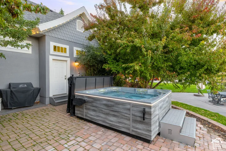 Exterior space featuring a hardscaped brick patio, a built-in hot tub with integrated lighting, shingle-style siding, and a concrete paver walkway