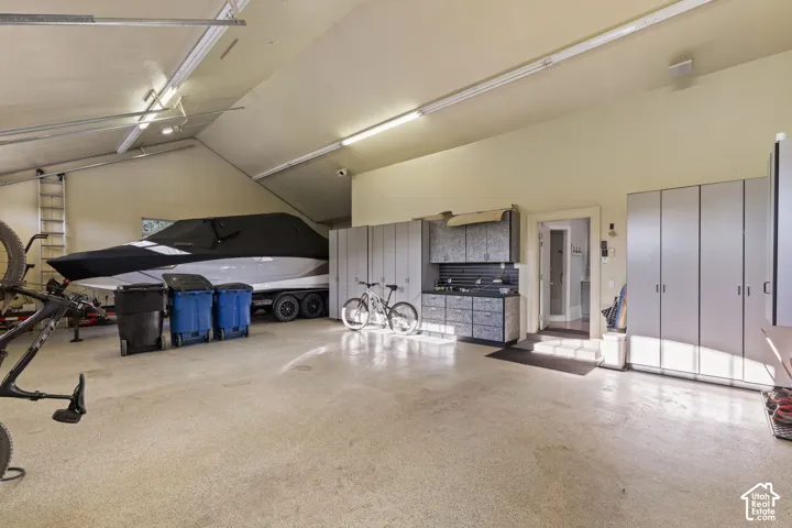 Spacious garage featuring high vaulted ceilings, durable epoxy flooring, custom built-in cabinetry, an integrated utility sink, and recessed LED lighting