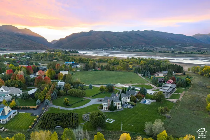 Extensive estate grounds featuring a hedge maze, paved circular driveway, stone exterior architecture, mountain backdrop, and proximity to water