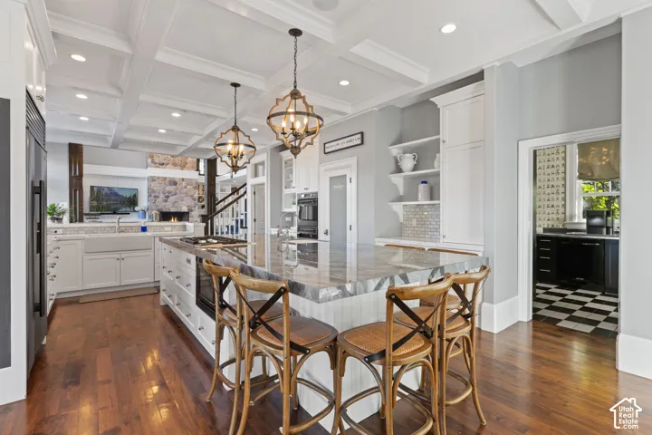 Kitchen featuring coffered ceilings, expansive center island with stone countertop, wood-finish flooring, custom built-in cabinetry, and integrated stainless steel appliances