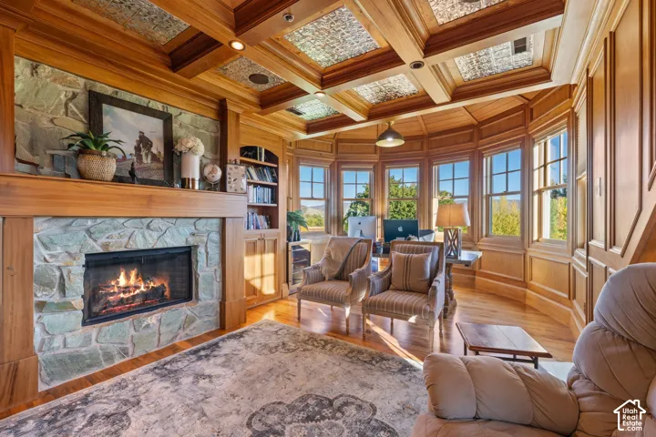 Wood-paneled room featuring a coffered ceiling with decorative inserts, a floor-to-ceiling stone fireplace surround, custom built-in cabinetry, and a multi-window bay configuration