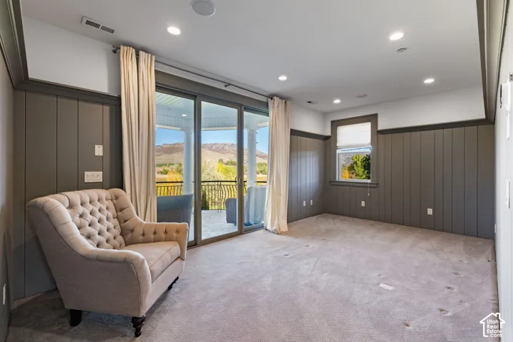 Interior space featuring full-height vertical paneling, recessed lighting, carpeted flooring, and glass sliding doors opening to an exterior balcony with mountain scenery