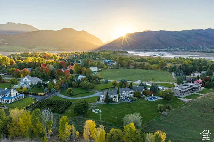 Aerial perspective of a multi-story residence featuring a circular driveway, an inground swimming pool, extensive lawn areas, and a mountain backdrop