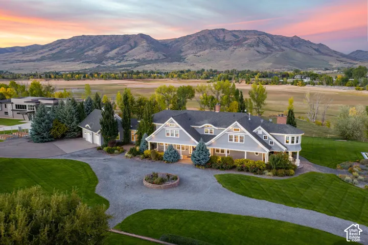 Lakefront residence with grey siding, expansive manicured grounds, circular stone-accented driveway, mature landscaping, and prominent mountain backdrop