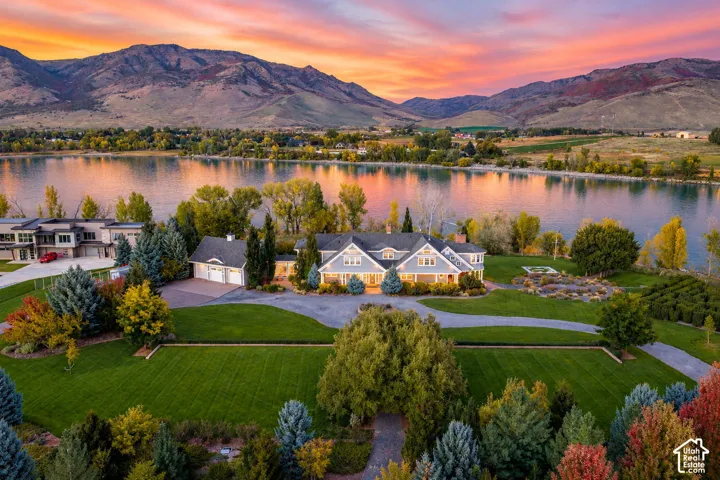 Waterfront property featuring a multi-gabled residence, attached multi-car garage, manicured lawn, and expansive mountain backdrop. Accurate AI generated depiction of the reservoir at full capacity. Currently drained for pipeline repair.