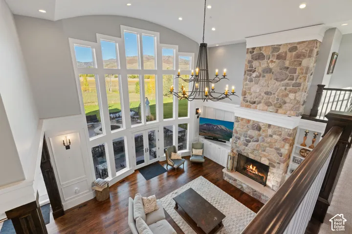 Double-height great room featuring a floor-to-ceiling multi-pane window wall, full-height stone fireplace, wood-finish flooring, custom built-in cabinetry, and a tiered iron chandelier
