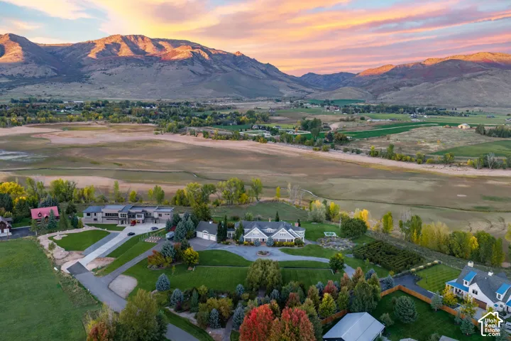 Aerial perspective of a multi-structure property featuring expansive manicured lawns, mature deciduous trees, a paved circular driveway, and a backdrop of prominent mountain ranges