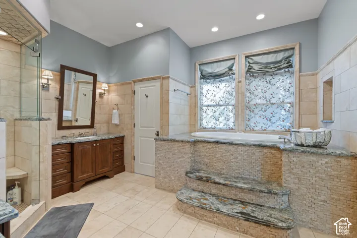 Bathroom featuring a stone-surround soaking tub with integrated stairs, custom wood cabinetry, stone tile wall accents, recessed lighting, and a glass-enclosed shower