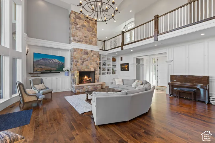Two-story living area featuring floor-to-ceiling stone fireplace, wood-finish flooring, custom built-in cabinetry, wrought iron chandelier, and a balcony with wood-accented railings