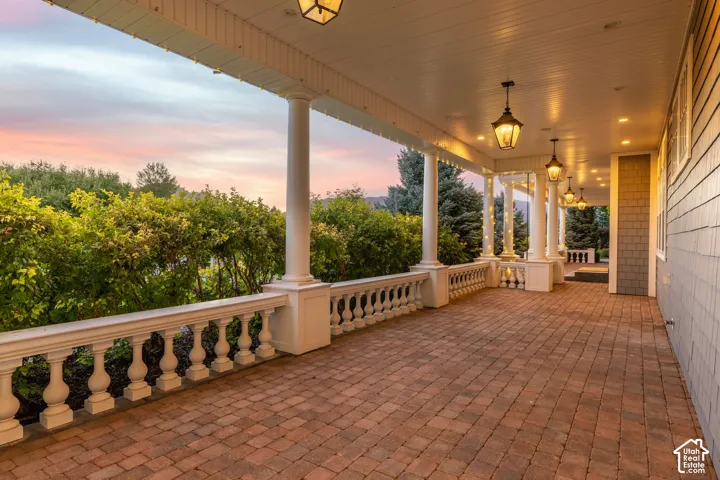 Covered veranda featuring decorative balustrade railings, architectural columns, brick-paver flooring, and hanging lantern-style fixtures