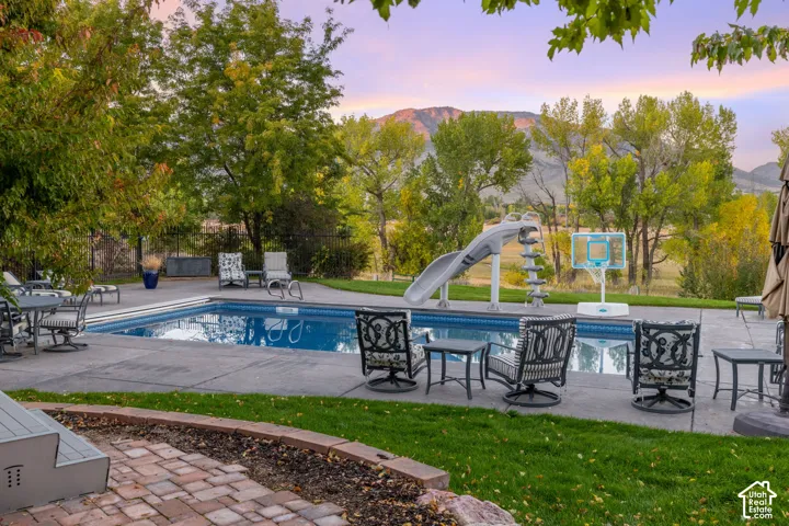 Outdoor space featuring an in-ground swimming pool with a slide, expansive concrete patio, brick hardscaping, and a mountain backdrop