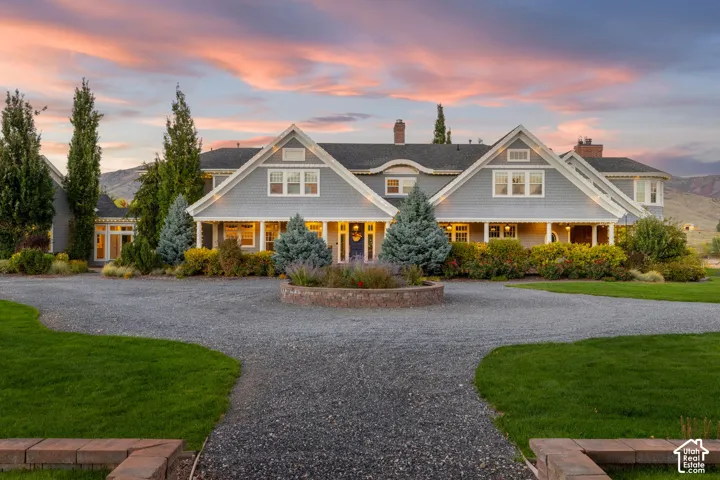 Shingle-style exterior featuring a circular driveway, multi-gabled roofline, stone-accented landscaping, and manicured lawn