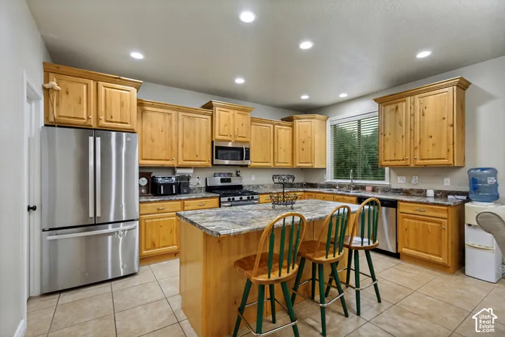 Kitchen featuring natural finish wood cabinetry, central island with stone-patterned countertop, stainless steel appliances, and tile flooring