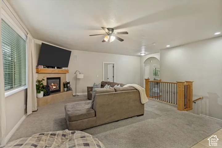 Fireplace with stone surround, wood mantel, ceiling fan with integrated lighting, recessed lighting, and staircase with wooden newel posts and metal balusters