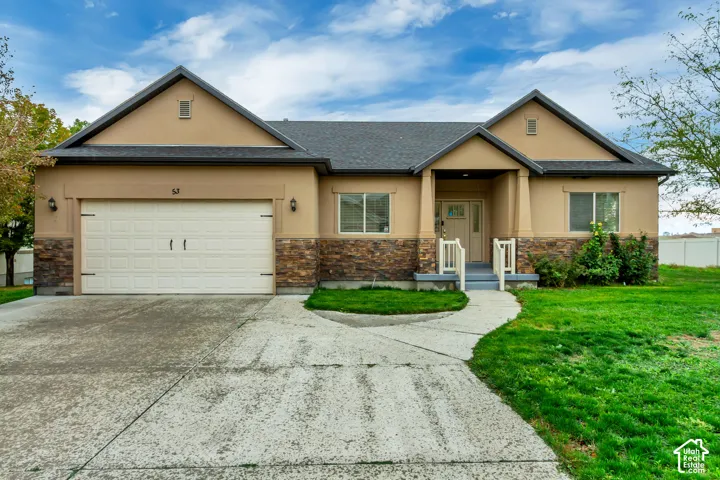 Single-level exterior featuring tan stucco siding, stone veneer accents, an attached two-car garage, and a covered front porch with tapered columns