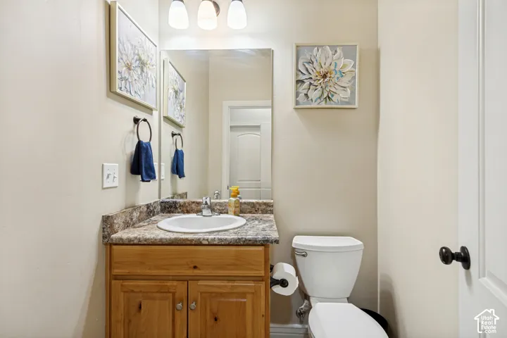 Vanity featuring a light wood-finish cabinet, stone-patterned countertop, integrated basin, and three-bulb vanity lighting fixture