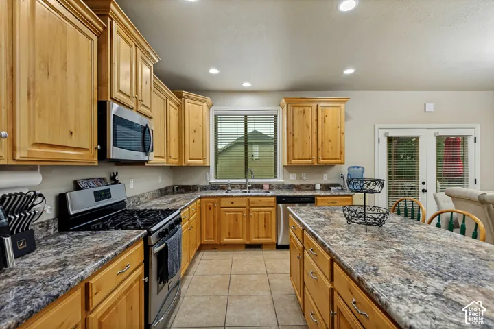 Kitchen featuring shaker-style wood cabinetry, stone-pattern laminate countertops, stainless steel appliances, ceramic tile flooring, and a central island