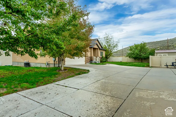 Exterior of the home featuring a concrete driveway, stone facade accents, multi-gabled roofline, and perimeter vinyl fencing against a mountain backdrop