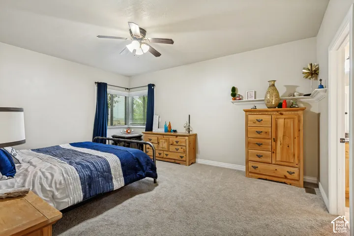 Neutral-toned interior featuring wall-to-wall carpeting, a corner window configuration, a built-in wall-mounted display ledge, and an overhead ceiling fan with integrated lighting