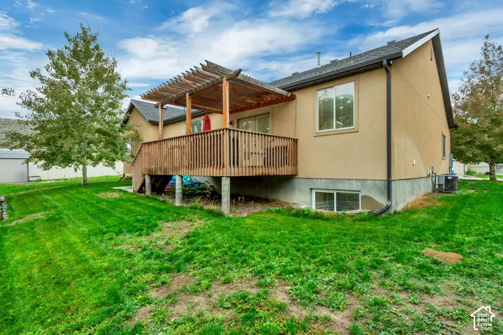 Rear exterior featuring a wood pergola, raised wood deck with vertical balusters, and expansive lawn area
